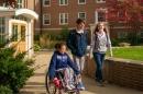 Three UNH students, 一个坐在轮椅上，两个站在她旁边, 在UNH的穆克兰大厅的院子里散步和开车.